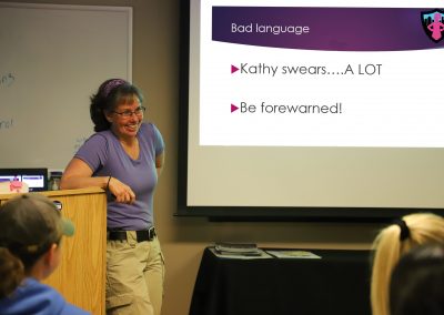 Kathy in front of a presentation slide with a warning that she swears "a lot!"